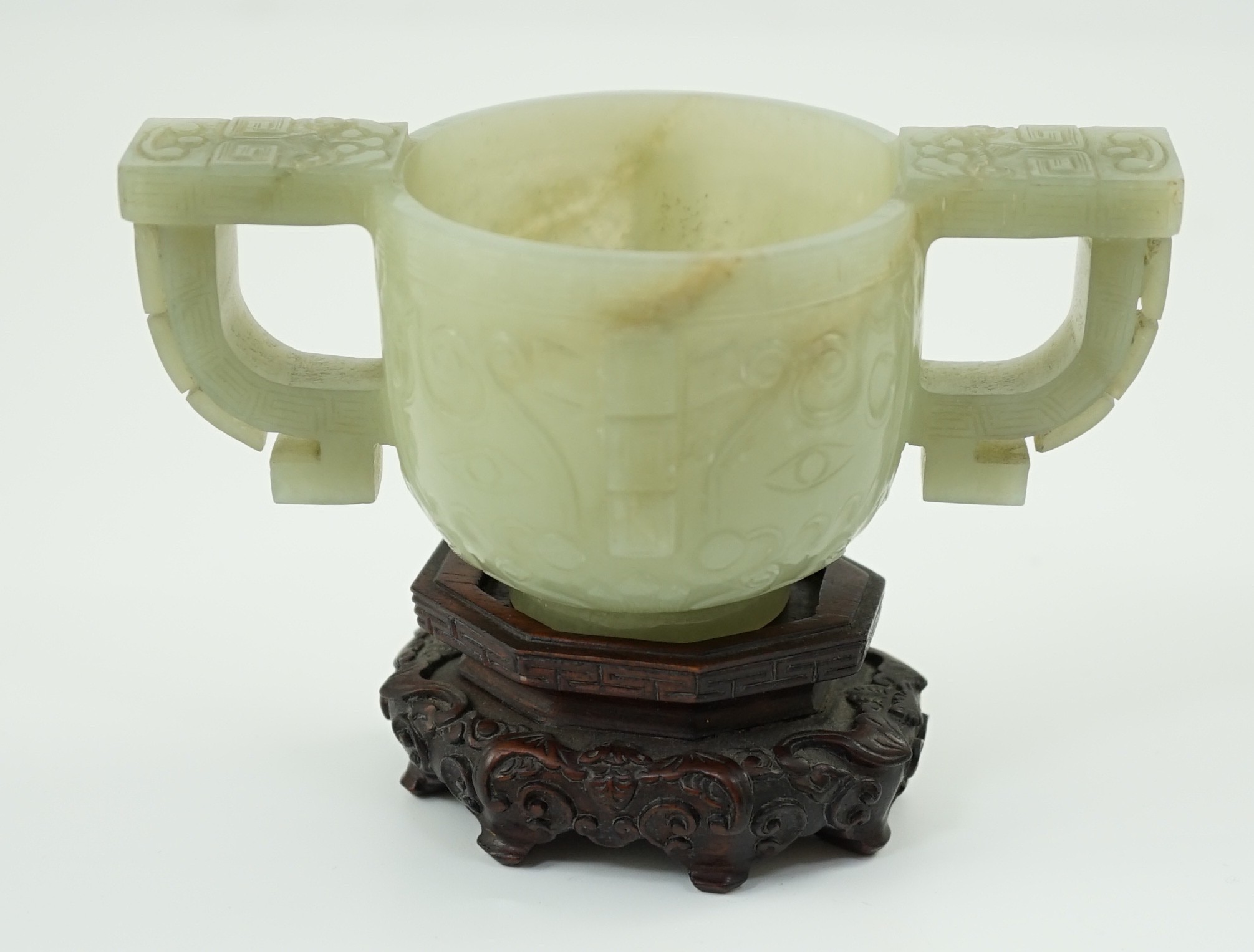 A Chinese archaistic celadon jade two handled cup, 17th century, 12.9cm across 6.1cm high, associated wood stand